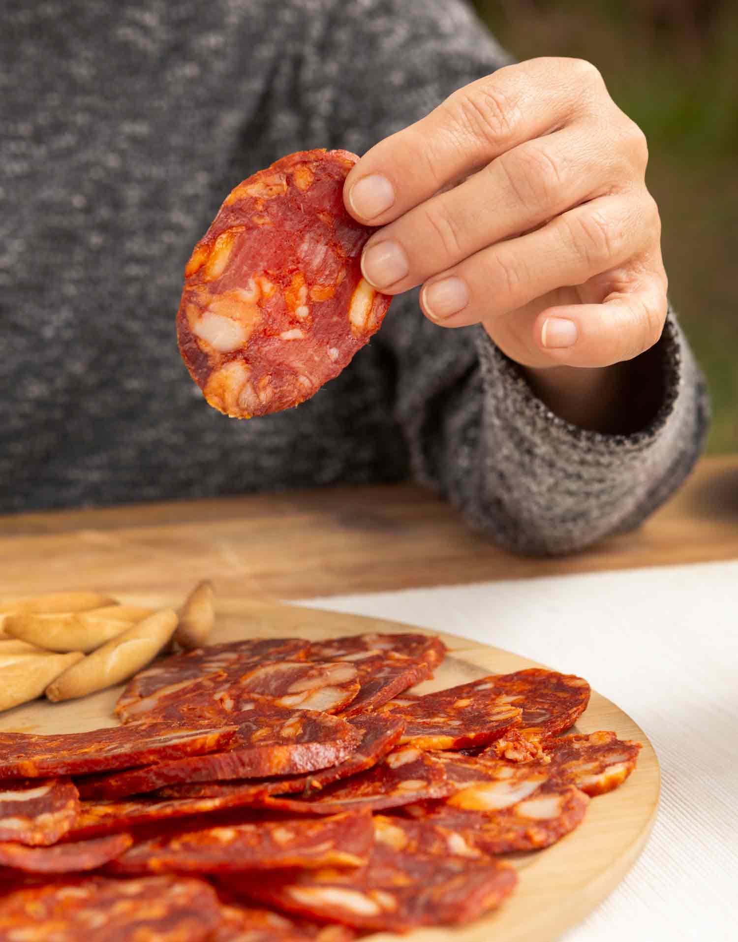 Persona sosteniendo una loncha de chorizo en primer plano sobre una mesa con más chorizo loncheado